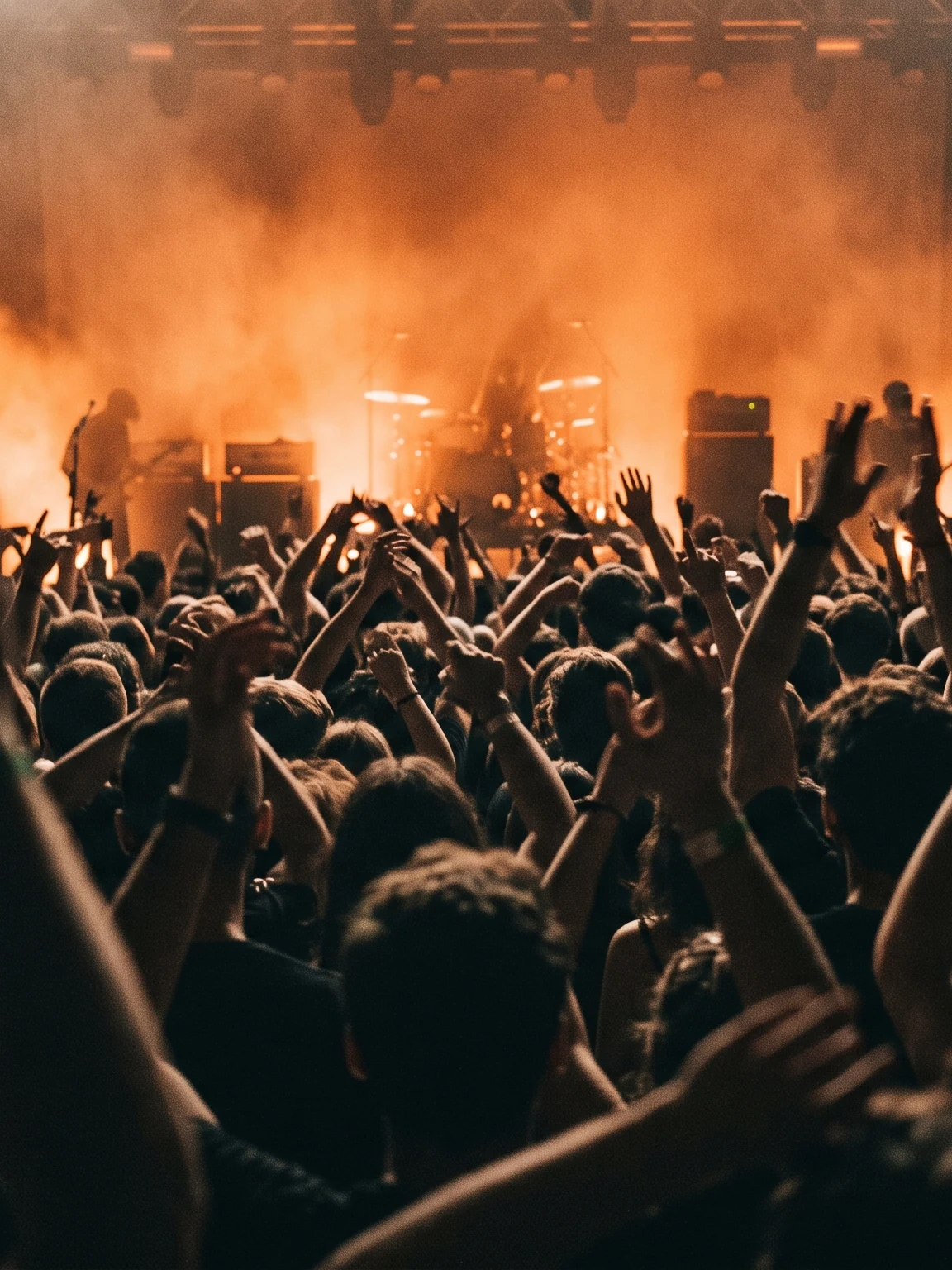 Crowd under orange stage light with hands raised